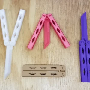 Four ForgeFi Butterfly Knives laid on a wooden surface, blunt printed balisongs shown open and closed with diamond cut-outs through the handles